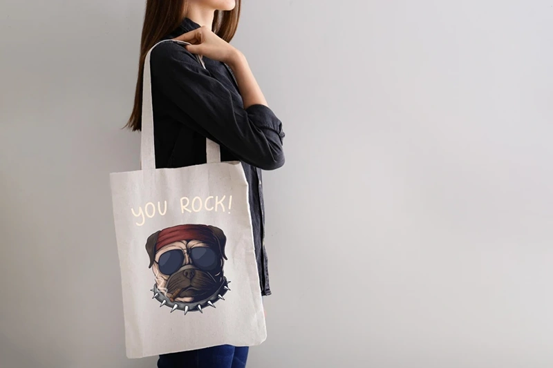 Naine heleda riidest ökokotiga õlal. Näide originaalsest koerapildist ja tekstist riidest kotil